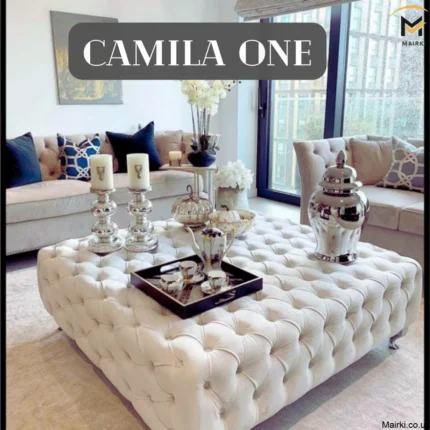 Elegant living room featuring a tufted ottoman with decorative items, a beige sofa, and large windows.