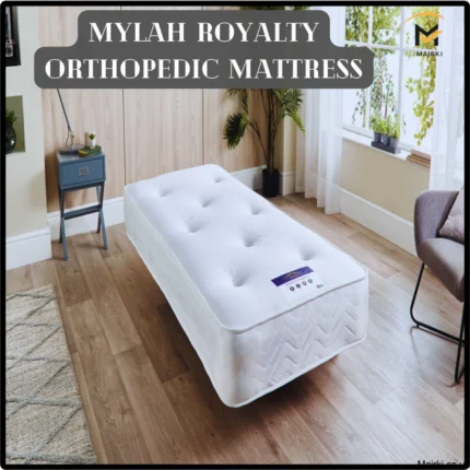 White orthopedic mattress in a bright room with wooden floor, potted plants, a side table, and a chair.