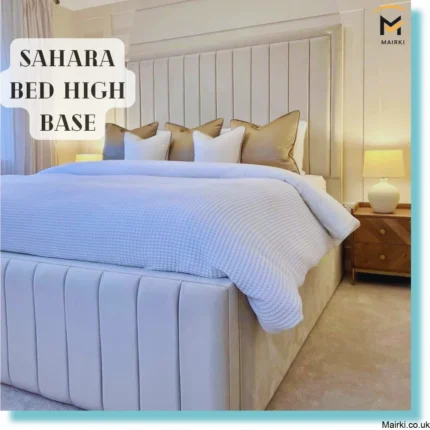 Luxurious bed with a high tufted base and upholstered headboard, featuring white and beige pillows and a wooden nightstand with a lamp.