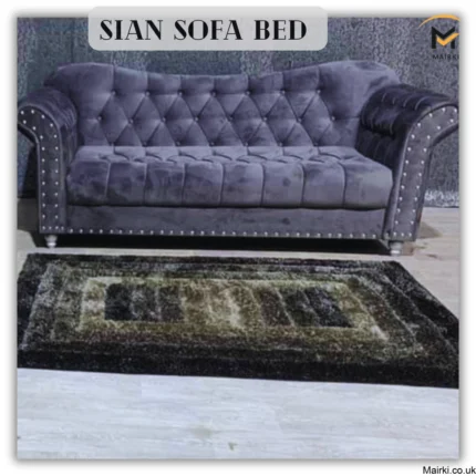 A dark gray sofa bed with studded arms and a patterned rug in front.