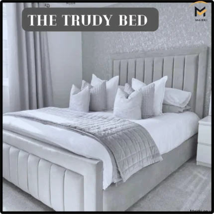 Luxurious gray and white bedroom featuring "The Trudy Bed" with a tall padded headboard and decorative pillows.