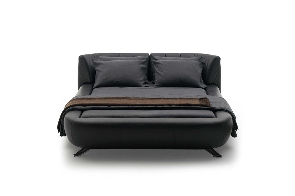 Black sofa bed unfolded with cushions and a throw blanket.