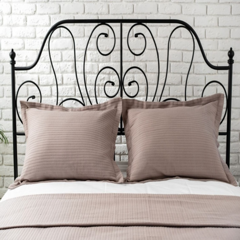 Black metal bed frame with decorative swirls, taupe pillows, and white brick wall.