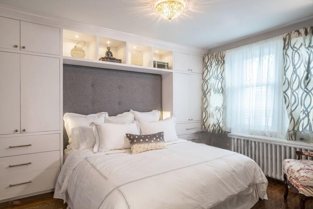 A bedroom with a bed featuring white linens and overbed storage with cabinets and shelves.