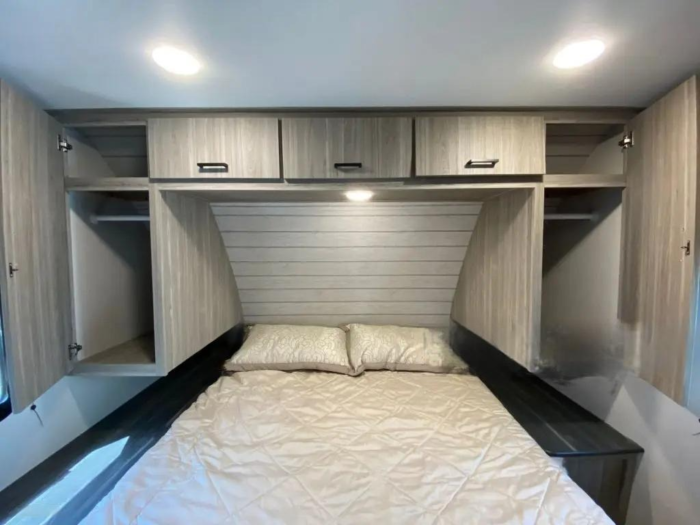 Bedroom with overbed storage including cabinets and open closets above a double bed with a cream quilt.