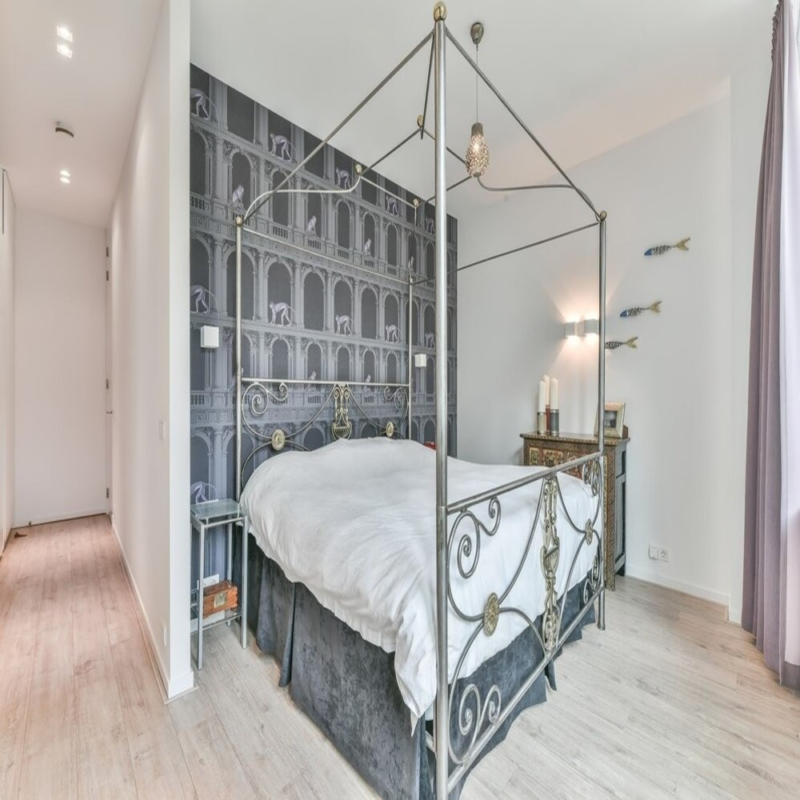 A bedroom with a Super King metal bed frame and a decorative gray wallpaper, featuring modern and ornate elements.