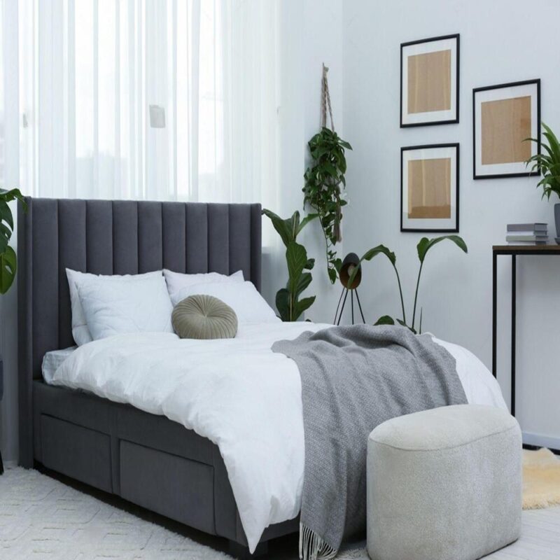 Modern bedroom with black ottoman bed, white bedding, and plants.