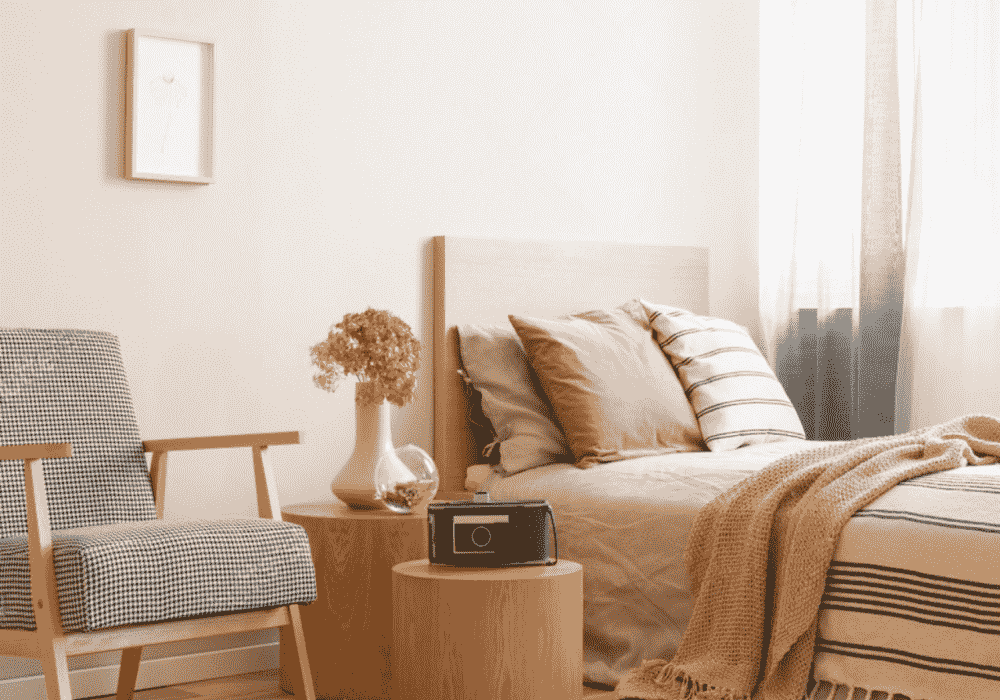 Cozy bedroom with a single wooden bed frame, houndstooth armchair, and side table with decor.